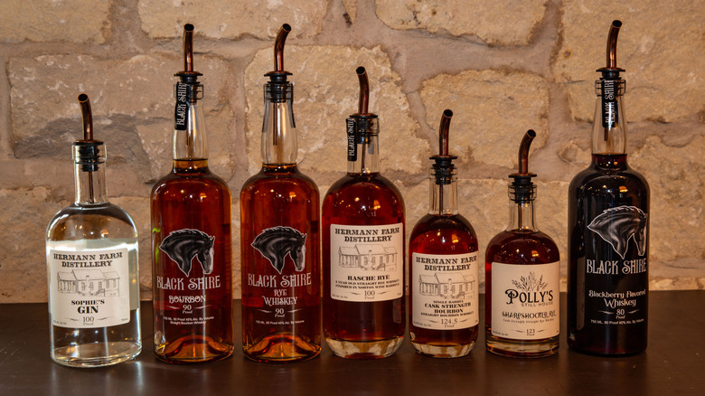 A lineup of bourbon bottles on wood surface with stonewall background.