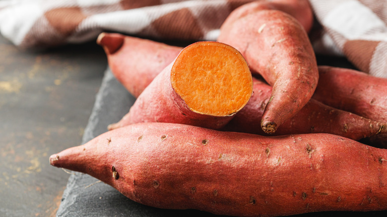 Several sweet potatoes on a table top, including one that has been cut in half