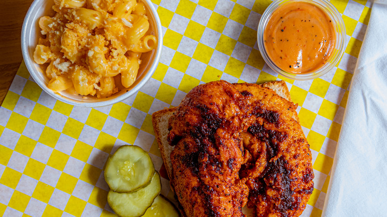 Spicy fried chicken, mac and cheese, sauce, and pickles on yellow gingham parchment paper