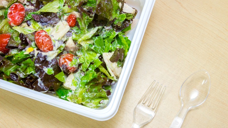 fast food salad in a takeout container next to plastic utensils