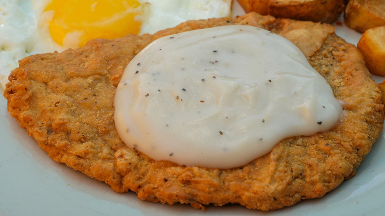 Country fried steak with white gravy on a plate.