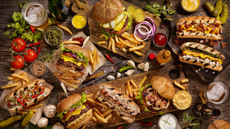 A very large spread of fast food that includes burgers, subs, hot dogs, and fries.