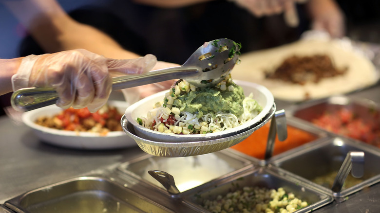 A chipotle employee scoops a spoonful of guacamole onto a burrito bowl