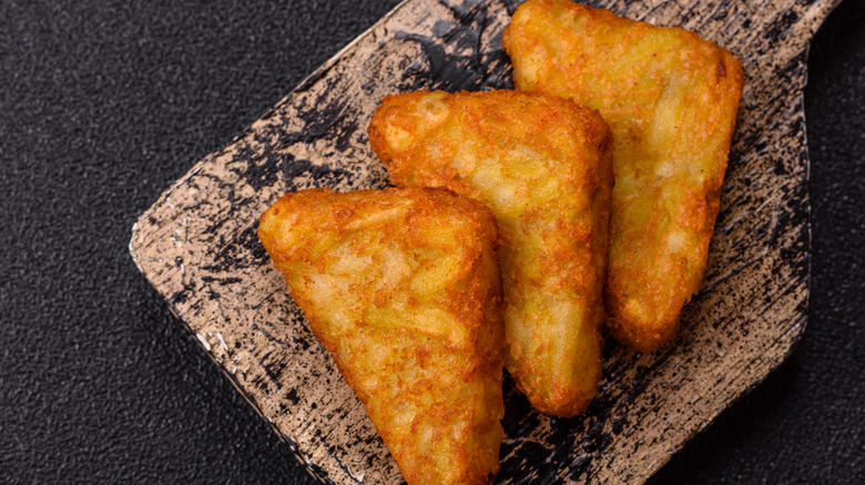 Macro closeup of breakfast or brunch potato fried two hash browns crispy texture on white plate with wooden table background