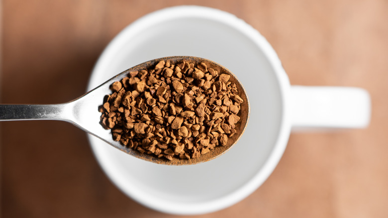A spoon of instant coffee held over an empty white mug