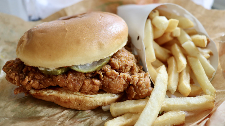 A fried chicken sandwich with pickles and a side of fries