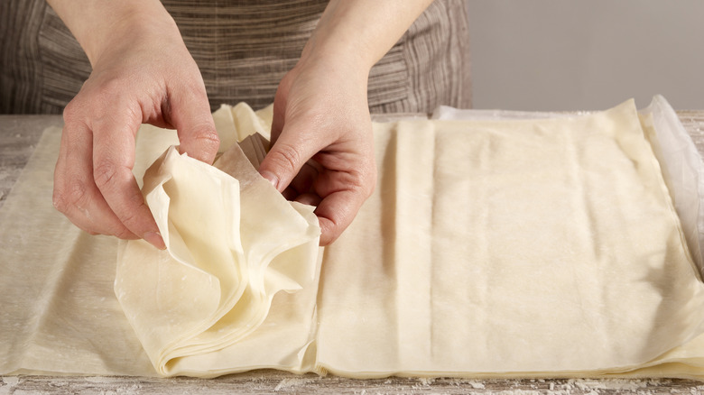 Hands peeling phyllo sheets apart