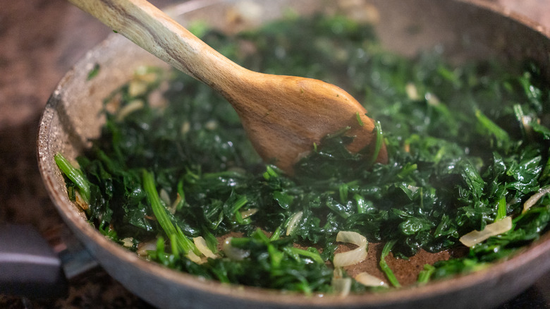 Spoon stirring sautéed greens in a pan