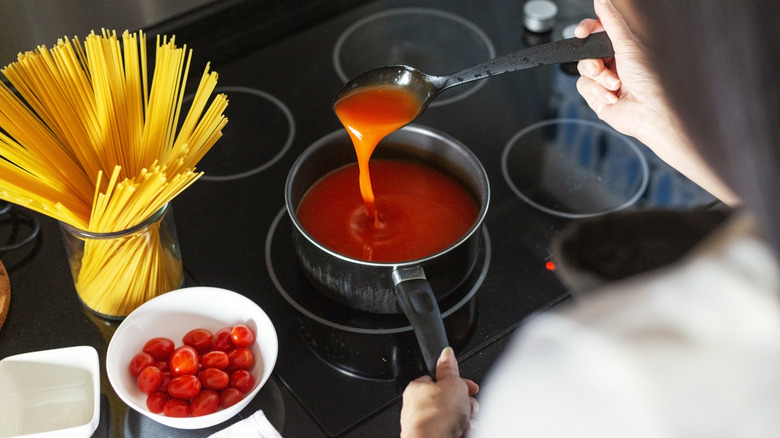 over the shoulder view of pasta sauce cooking, cherry tomatoes and spaghetti on the side