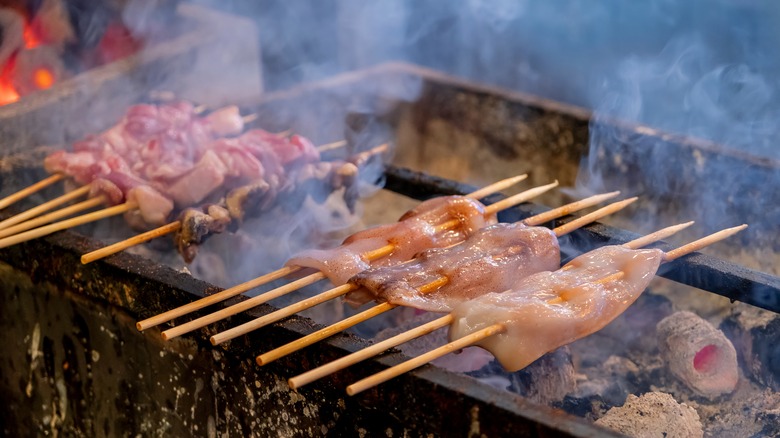 A couple of beef skewers grilling over charcoal