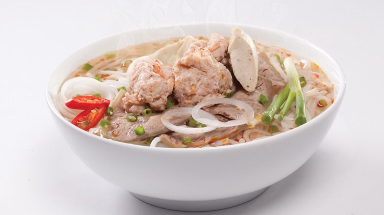 A steaming hot bowl of bún bò huế against a white background
