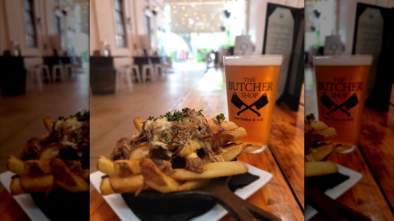 Pulled pork cheese fries and a beer in a The Butcher Shop Beer Garden & Grill branded pint glass