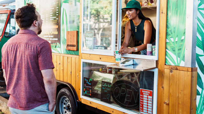 a caucasian man ordering food from food truck window where asian woman is working