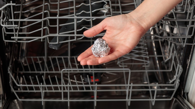 Person placing aluminum foil into a dishwasher.
