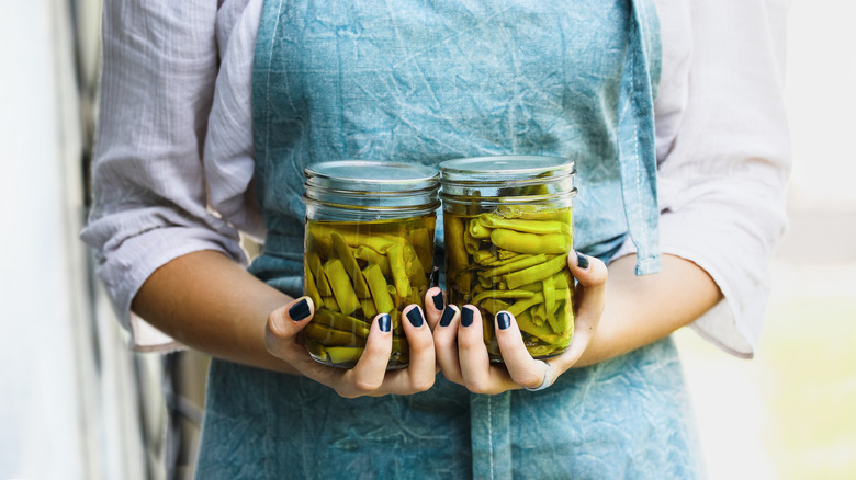 Young woman in a linen apron holding two mason jars filled with fresh home grown green beans.