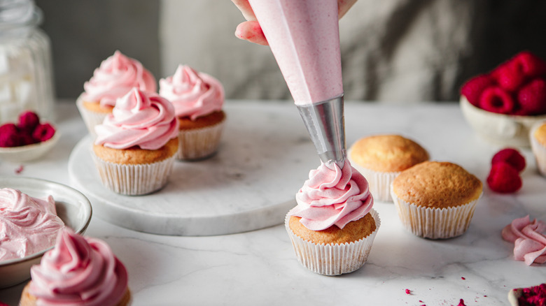 Person frosting a batch of cupcakes with pink frosting