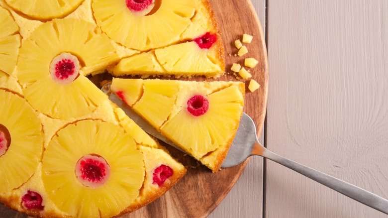 Slice being lifted from a pineapple upside down cake on a wooden board