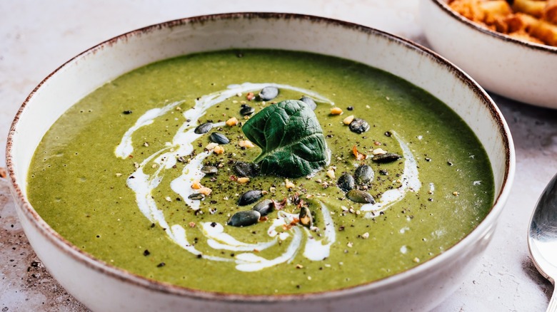 A bowl of green goddess soup garnished with pepitas in a white dish