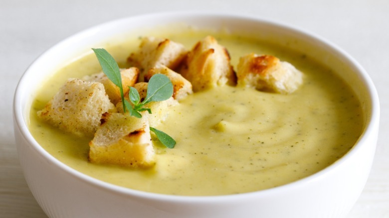 A bowl of cream of leek soup with a crouton garnish in a white bowl against a cream background.