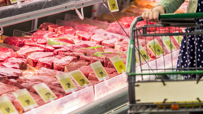 Woman shopping for raw meat in meat department of grocery store.