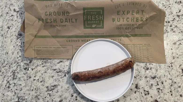 Sausage from The Fresh Market on a white plate with the branded paper deli bag