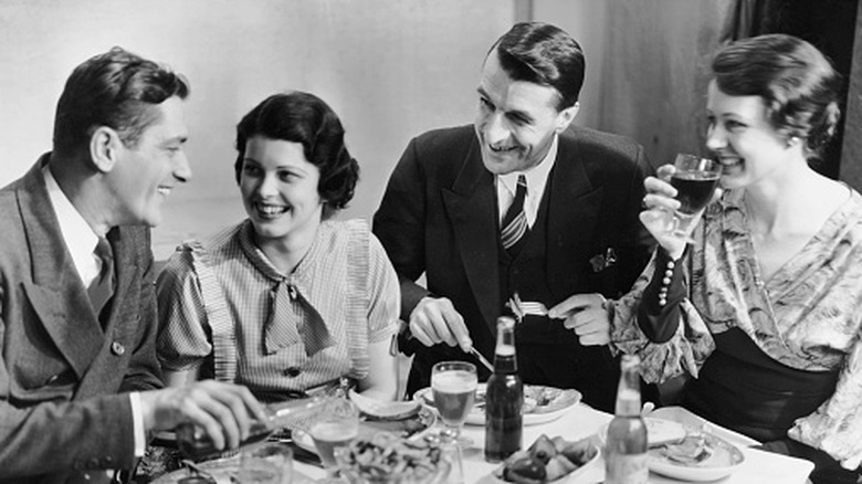 Black and white photo of two couples sitting at a dinner table in 1950s-style attire.