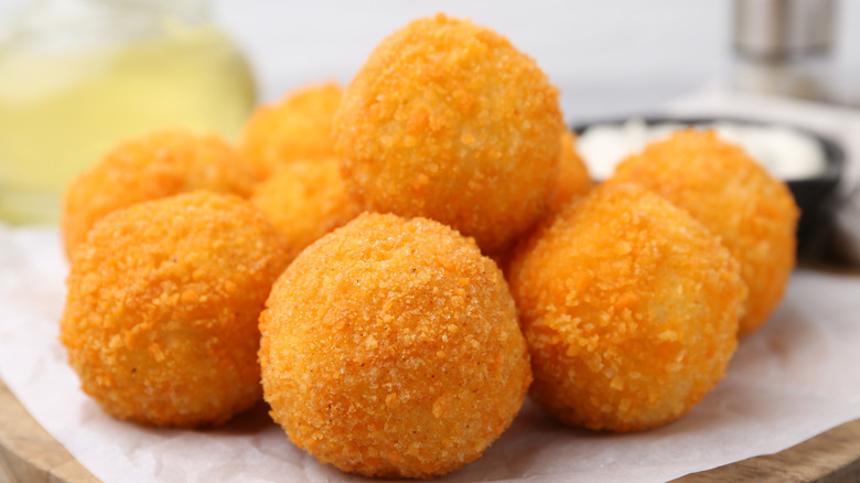 Fried croquettes on a piece of parchment paper on a cutting board with a ramekin of white sauce in the background.