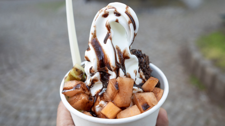 A cup of frozen yogurt covered in toppings and chocolate sauce
