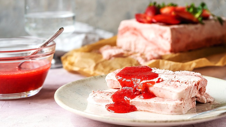 Sliceable frozen and creamy strawberry dessert covered in strawberry sauce on a cream-colored plate