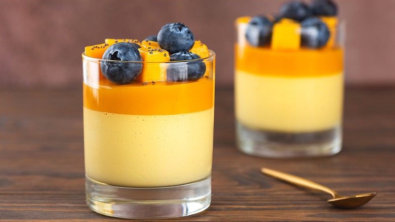 Layered mango-flavored dessert in two short glasses topped with fresh cubes of mango and whole blueberries