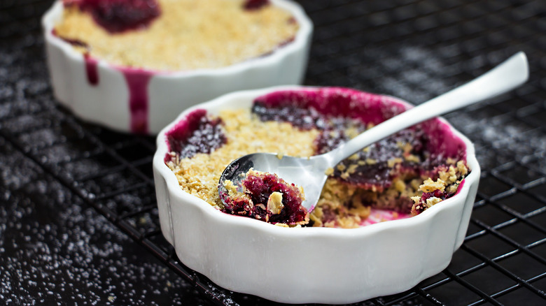 Two ramekins of blueberry crumble with a spoon