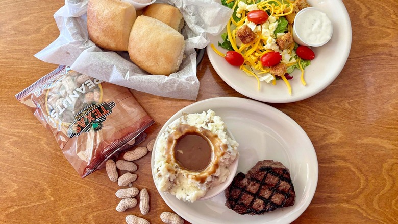 Texas Roadhouse salad, steak with mashed potatoes, peanuts, and rolls on a table