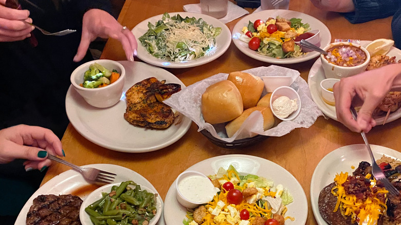 People's hands holding forks and eating from an assortment of plates at Texas Roadhouse
