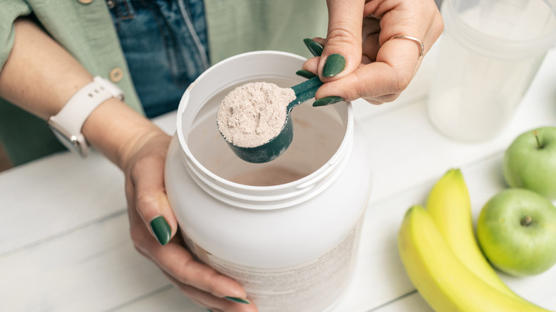 person scooping protein powder from a large container