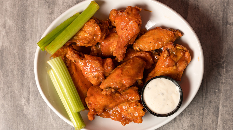 A plate of Buffalo wings with celery sticks and a creamy dipping sauce.