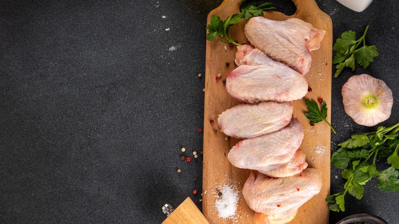 Raw chicken wings lined up on a wooden cutting board.