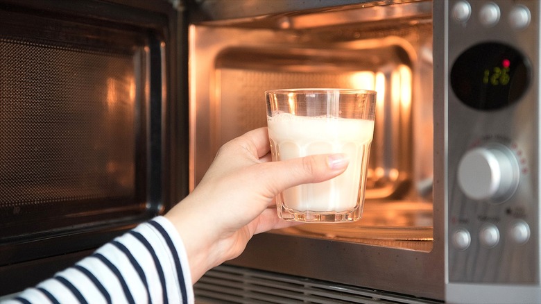 Hand placing a glass of milk in a microwave