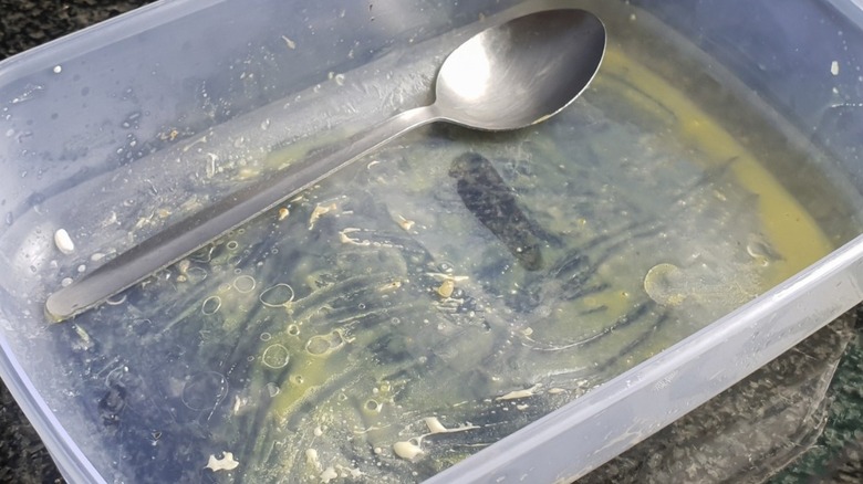 A dirty plastic food container with a spoon inside it ready to be washed and cleaned.