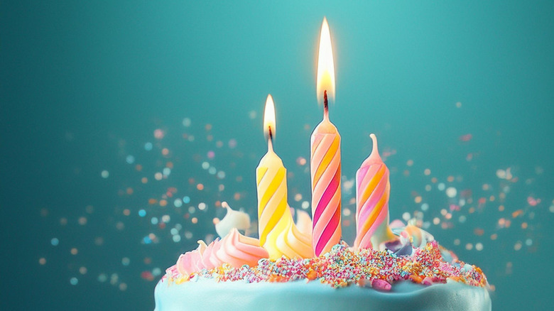 Frosting has been poured over a birthday cake topped with sprinkles and three candles.