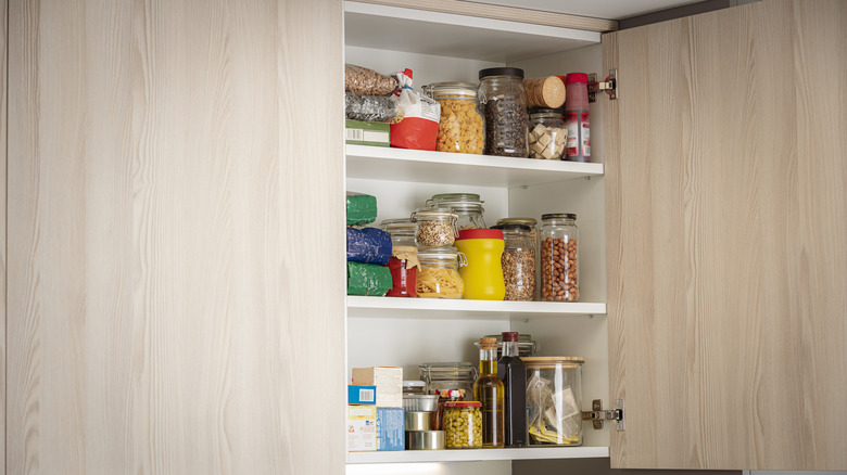 An open kitchen cabinet with jars and other containers inside.
