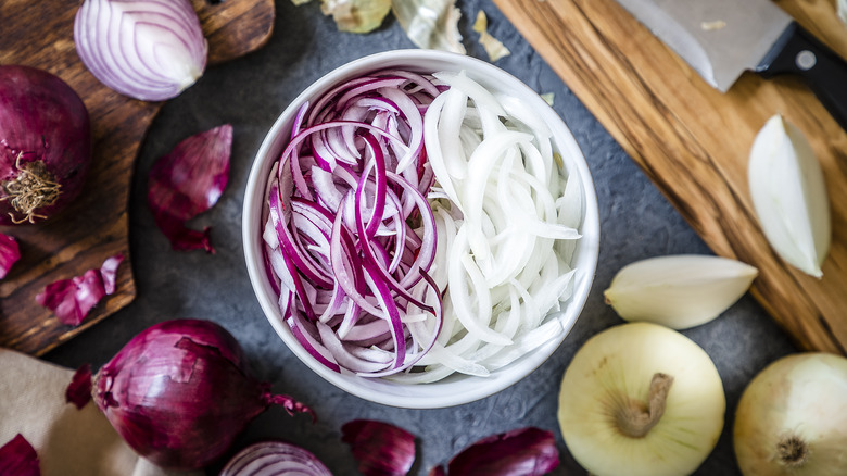A bowl of sliced onions on a gray surface.