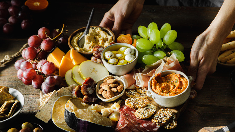 Charcuterie board with cheeses, fruits, and bowls of spreads on a table.