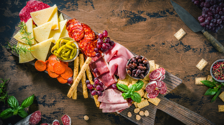 A charcuterie board filled with meats, cheeses, olives, grapes, peppers, and crackers.