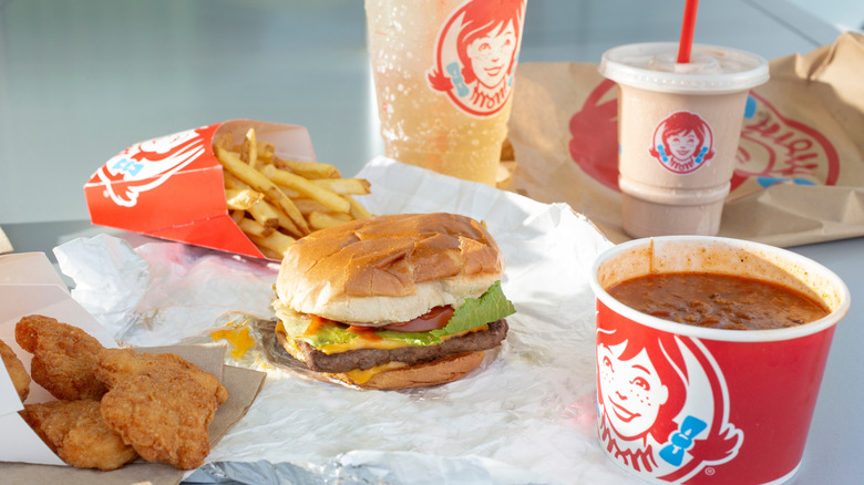 Burger, fries, chicken nuggets, chili, drink, and a Frosty from Wendy's arranged on a table