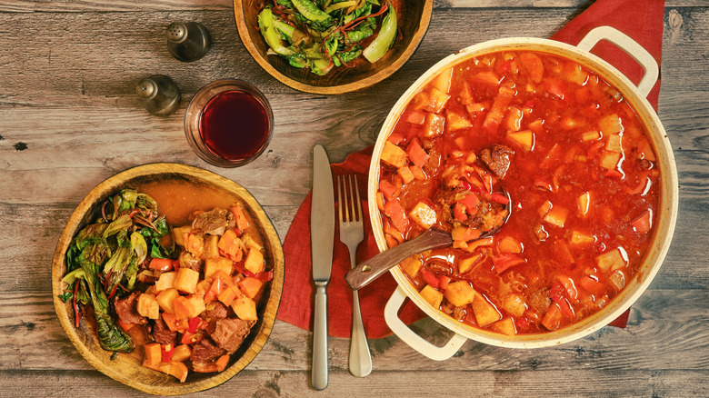 Homemade simple stew in a pot and bowls on wood