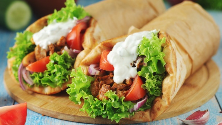 Two gyro sandwiches in pita bread on a wood plate looking similar to tacos.