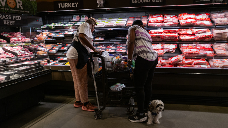 Grocery shoppers choosing meat from a cold case.