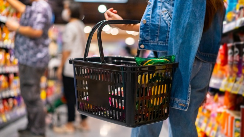 A grocery shopper carrying a black plastic basket.