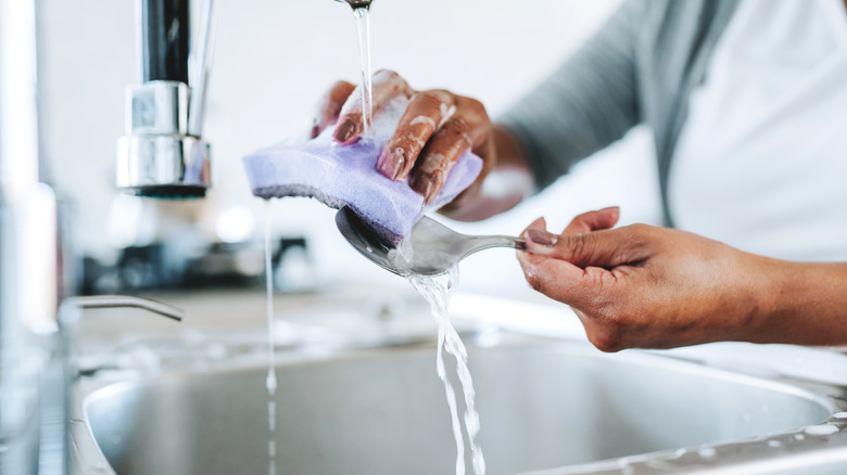 Person washing a spoon with a kitchen sponge