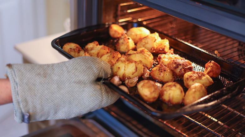 A gloved hand removing a pan of roasted potatoes from an oven
